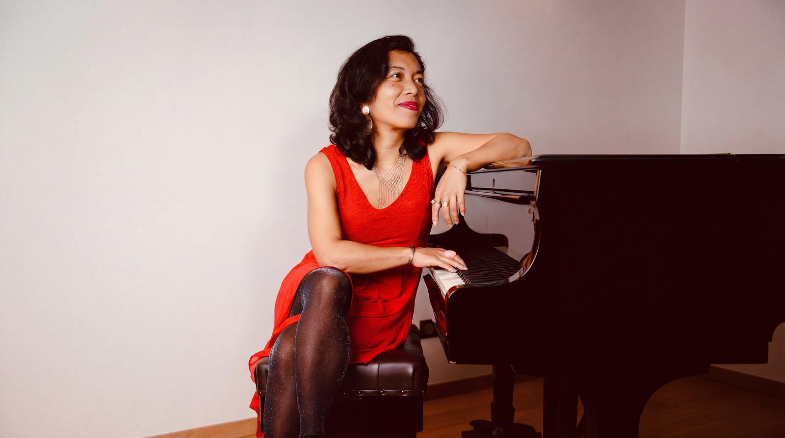 Jinja Andrianambinina-Teyssier, en robe rouge, assise au piano à queue